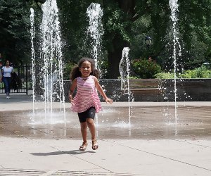 Girl runs through the sprinklers at the East 110th Street Playground