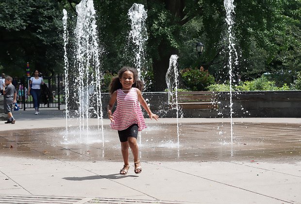 Girl runs through the sprinklers at the East 110th Street Playground